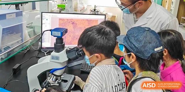 A student in a mask using a microscope during a science class or lab at Shanghai High School International Division.