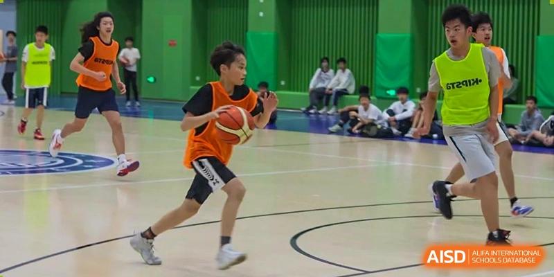 A young student in an orange jersey dribbling a basketball during a game at Shanghai High School International Division.