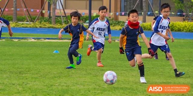 Students running and chasing a soccer ball on a grassy field at Shanghai High School International Division.