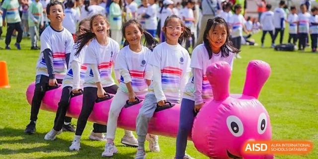 A group of female students smiling while sitting on large pink inflatables during an outdoor school event at Shanghai High School International Division.