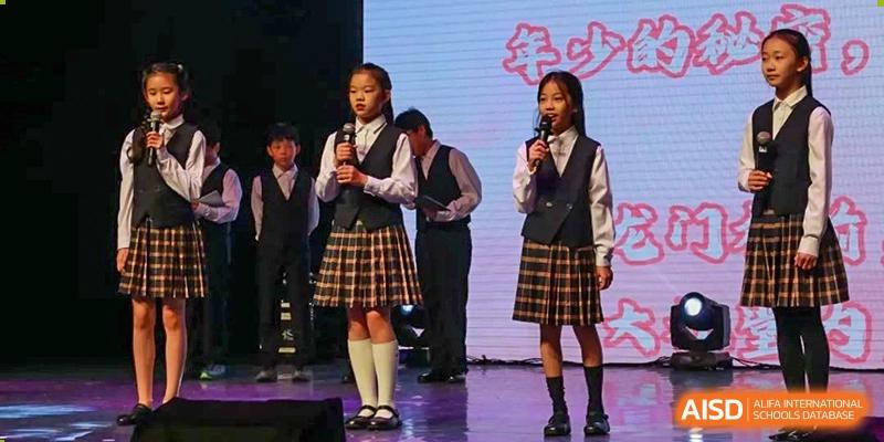 Two female students in school uniforms speaking or singing into microphones on a stage during a performance at Shanghai High School International Division.