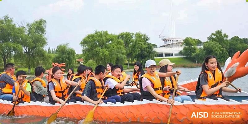 Students wearing life vests paddling a large inflatable boat on the water during an outdoor activity at Shanghai High School International Division.