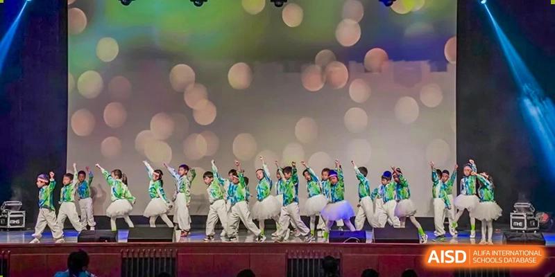A group of students performing a synchronized dance routine on a stage with blurred lights in the background at Shanghai High School International Division.