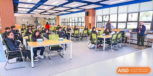 Students from Shanghai Qibao Dwight High School sit in a modern classroom, working on laptops in groups.