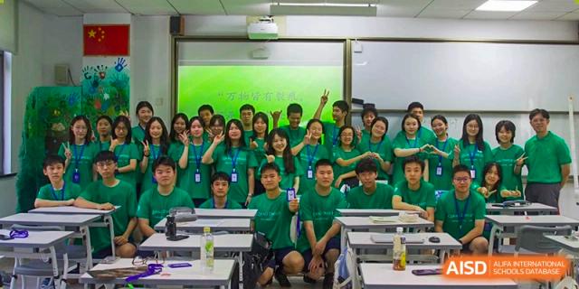 A group of students from Shanghai Qibao Dwight High School wearing green shirts pose for a photo in a classroom.