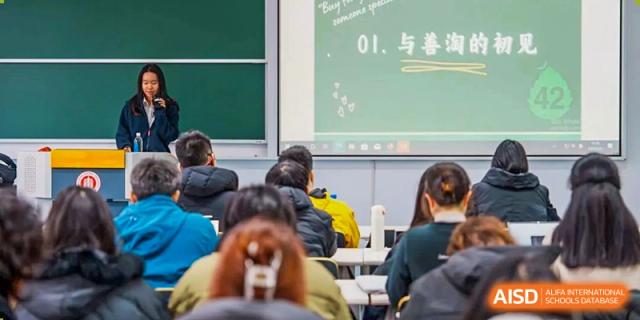 Students from Shanghai Qibao Dwight High School sit at desks in a classroom, listening to a teacher.