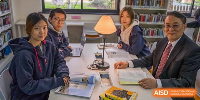 Students from Shanghai Qibao Dwight High School study together at a table with a lamp.