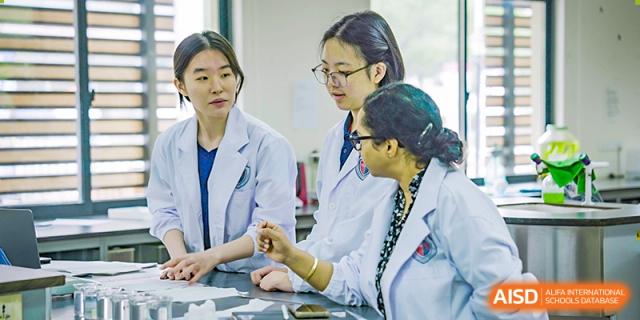Shanghai Qibao Dwight High School students in lab coats collaborating and looking at something on a table.