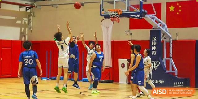 Basketball players from Shanghai Qibao Dwight High School stand on the court, one of them shooting a basketball toward the hoop.