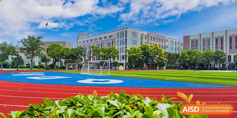 The exterior of the Shanghai Qibao Dwight High School building, with a running track and soccer field in the foreground.