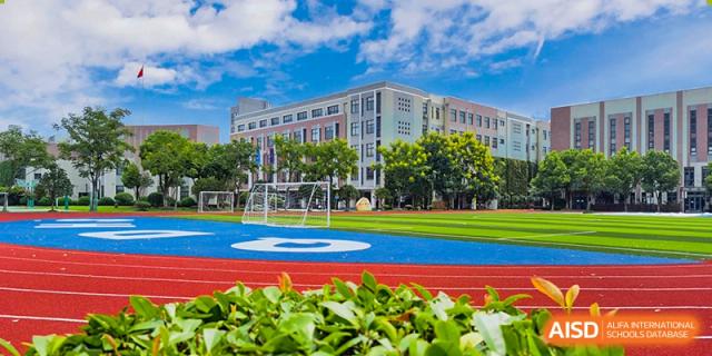 The exterior of the Shanghai Qibao Dwight High School building, with a running track and soccer field in the foreground.