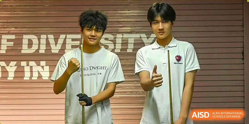 Two students from Shanghai Qibao Dwight High School, one wearing a fencing glove and one with a thumbs-up, pose together.
