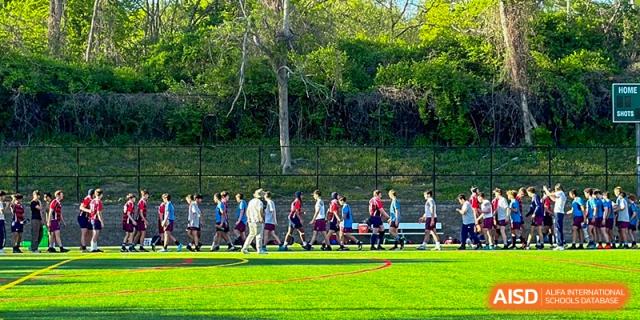 Students from Shanghai Qibao Dwight High School walk in a large group on a grassy field.