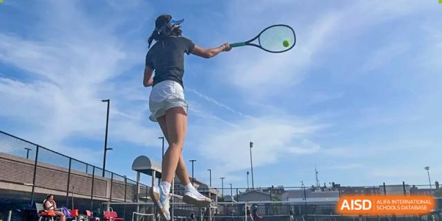 A female student from Shanghai Qibao Dwight High School is shown from behind as she hits a tennis ball.