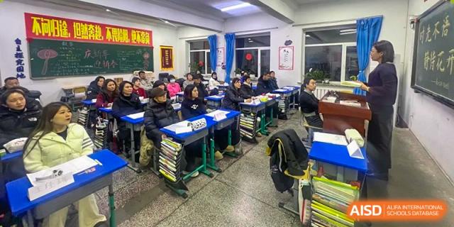 Students and possibly parents seated at desks in a classroom during an evening gathering or class at Shenyang Feiyue Experimental School.