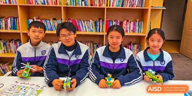 Two students sitting together at a table with a backdrop of bookshelves, showcasing their robotic creations at Shenyang Feiyue Experimental School.