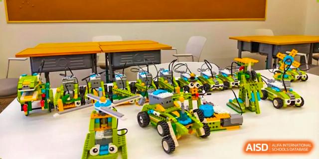 Several student-built robots or models made with green and black components displayed on a table in a classroom or lab at Shenyang Feiyue Experimental School.