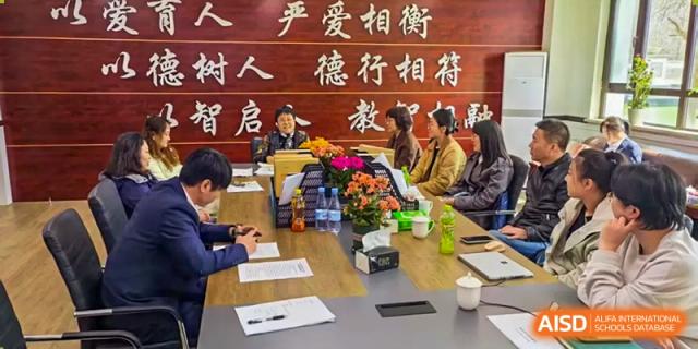 Teachers and administrators in a meeting around a table with Chinese text on the wall in the background at Shenyang Feiyue Experimental School.