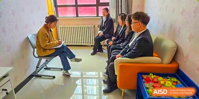 A group of adults in professional attire sitting in a row, possibly for a meeting or interview, at Shenyang Feiyue Experimental School.