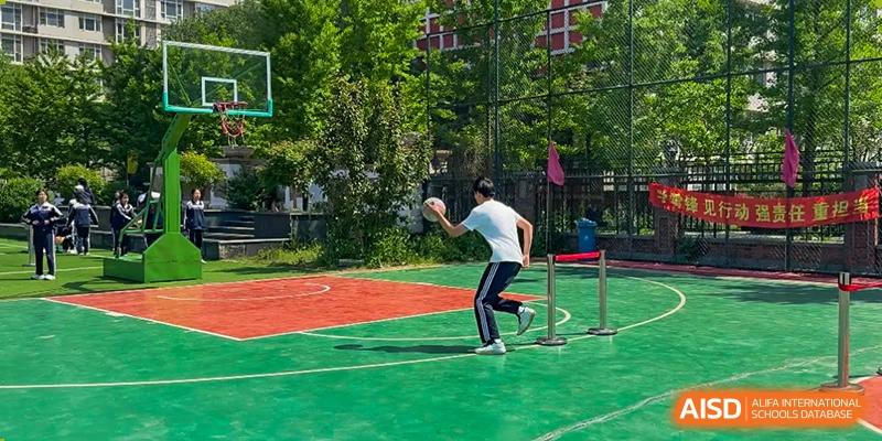 A student throwing a shot put or similar object on a red and green sports court at Shenyang Feiyue Experimental School.