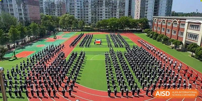 An aerial view of a large group of students in formation on a green sports field or track for an assembly or event at Shenyang Feiyue Experimental School.