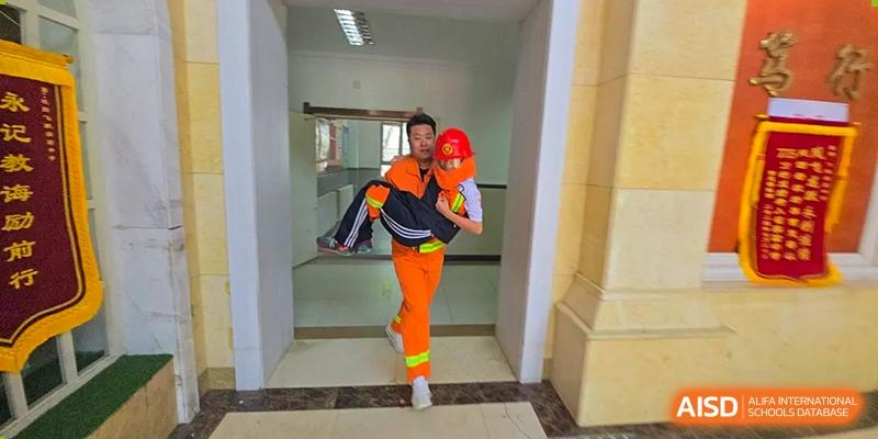 A student or staff member in an orange uniform carrying another person in a rescue drill inside a building at Shenyang Feiyue Experimental School.