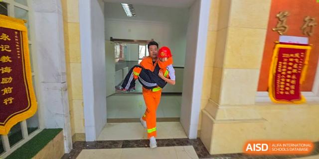 A student or staff member in an orange uniform carrying another person in a rescue drill inside a building at Shenyang Feiyue Experimental School.