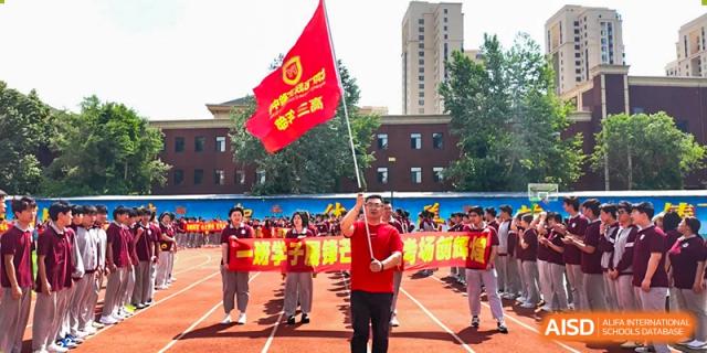 A group of people, including a man holding a red flag, participating in a school event or parade at Shenyang Feiyue Experimental School.