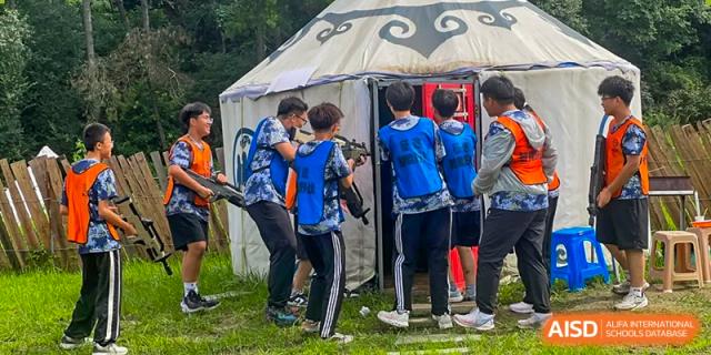 Students participating in a team-building or laser tag activity near a yurt-like tent structure at Shenyang Feiyue Experimental School.