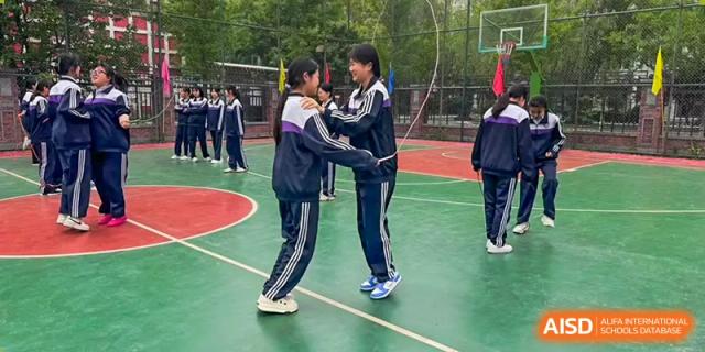 Two students in school uniforms shaking hands or embracing on an outdoor basketball court at Shenyang Feiyue Experimental School.