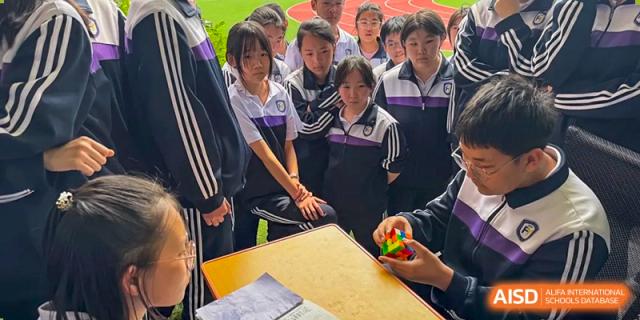 A close-up of students in uniform gathered around a table with a Rubik's Cube during a classroom or club activity at Shenyang Feiyue Experimental School.