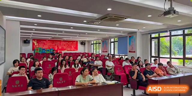 An indoor meeting or lecture with a large audience seated in rows of red chairs, facing the front of the room at Shenyang Feiyue Experimental School.