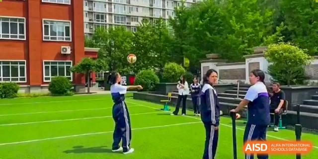 A student in uniform preparing to hit a ball during an outdoor sports activity on a green turf field at Shenyang Feiyue Experimental School.