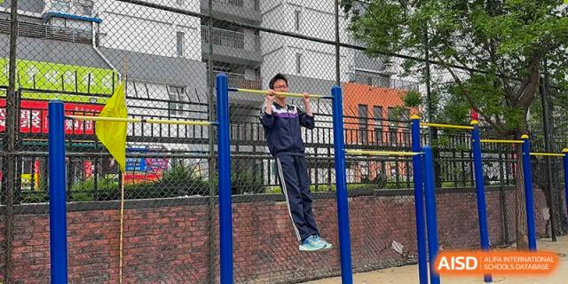 A student doing a pull-up or hanging on a bar during physical activity at Shenyang Feiyue Experimental School.
