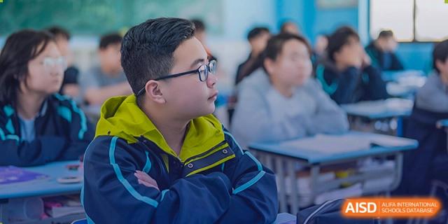 A male student wearing glasses and a jacket, focused on a lesson in a classroom at Sino-Canada School.
