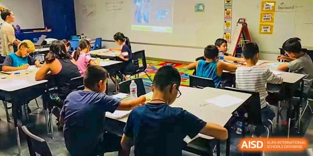 A classroom of students is actively engaged in a lesson, with one student in the foreground working on a laptop at Sino-Canada School.