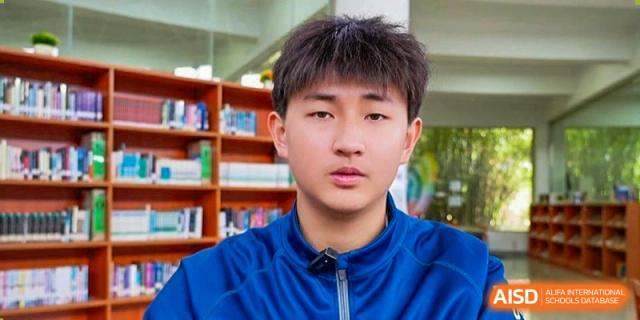 A young male student is looking directly at the camera while standing in front of a bookshelf at Sino-Canada School.