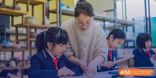 A teacher from Sino-Canada School patiently helping two young students with a hands-on activity.