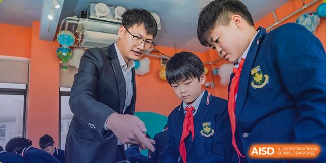 A male teacher from Sino-Canada School helping two male students with their classwork.