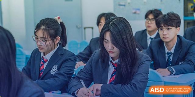 A female student from Sino-Canada School sitting at a desk and writing in a notebook during class.