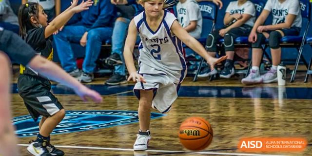 A young boy in a basketball uniform dribbles a basketball during a game at Sino-Canada School.