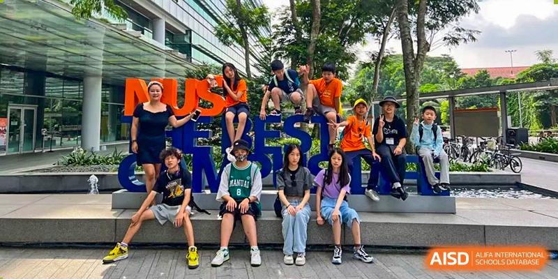 A group of students from Sino-Canada School are sitting on and in front of a large, blue sculpture outdoors.