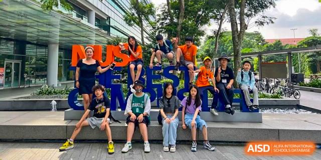 A group of students from Sino-Canada School are sitting on and in front of a large, blue sculpture outdoors.