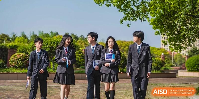 A group of three students in school uniforms holding books and posing for a photo at Sino-Canada School.