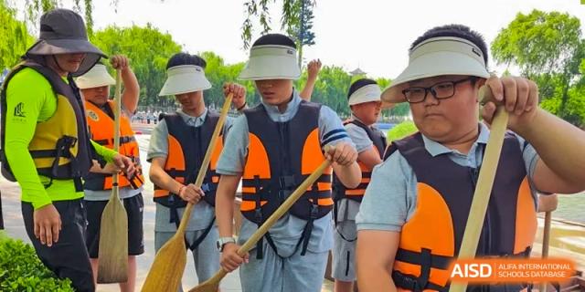 A group of students wearing life vests and helmets, holding paddles for a water activity at Sino-Canada School.