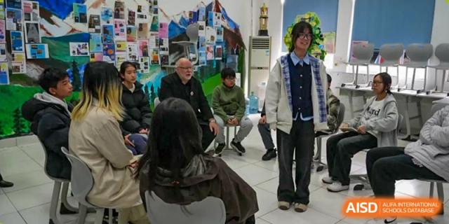 A student in a classroom setting, standing while others sit and talk with an adult at Sino-Canada School.
