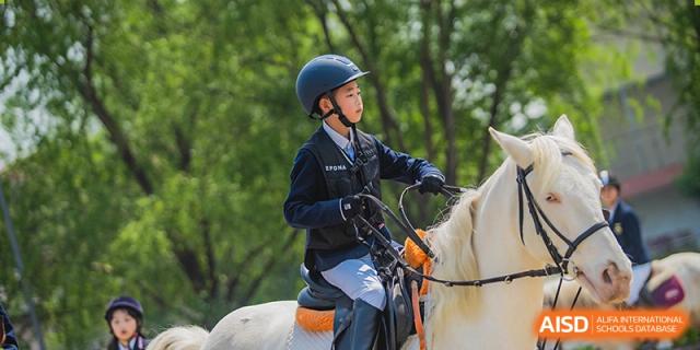 A young student in a helmet and riding gear is on horseback at Sino-Canada School.