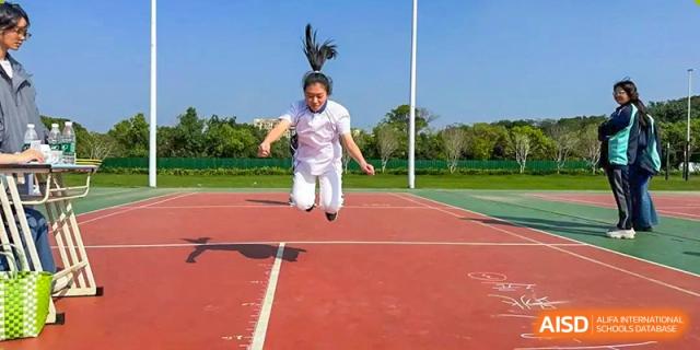 A student is captured mid-air during a long jump or high jump on a track field at Sino-Canada School.