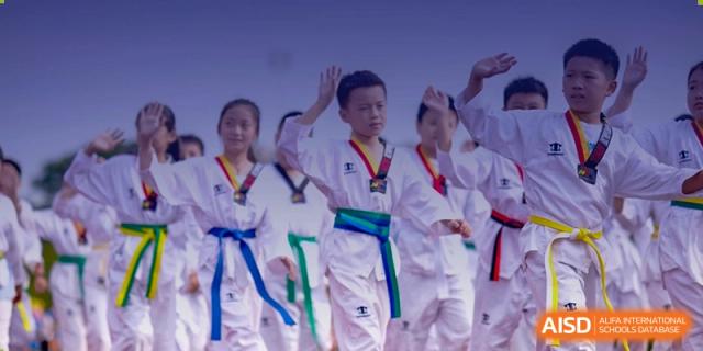 A group of students in white uniforms with different colored belts are practicing martial arts at Sino-Canada School.