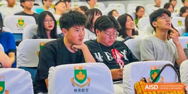 A student in the audience with a Sino-Canada School banner in front of him, attentively watching an event.